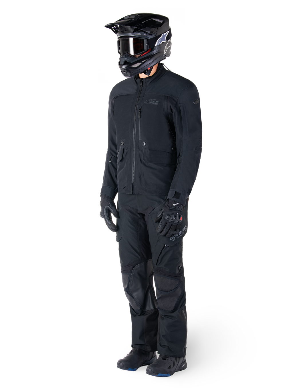 Motociclista che indossa la giacca Alpinestars St-7 Prime GORE-TEX in nero, completo coordinato da adventure touring con pantaloni neri abbinati, casco nero con maschera e guanti, caratterizzato da un design essenziale e funzionale per prestazioni in ogni condizione atmosferica.