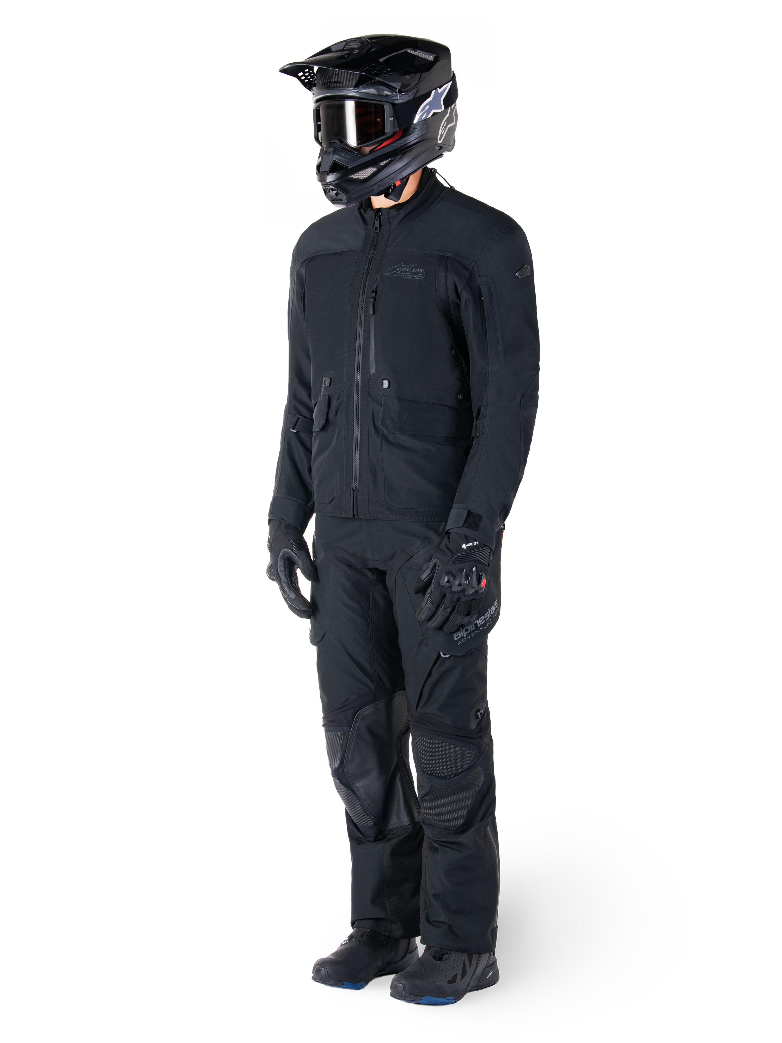 Motociclista che indossa la giacca Alpinestars St-7 Prime GORE-TEX in nero, completo coordinato da adventure touring con pantaloni neri abbinati, casco nero con maschera e guanti, caratterizzato da un design essenziale e funzionale per prestazioni in ogni condizione atmosferica.