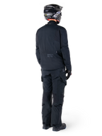 Vista posteriore di un pilota con giacca Alpinestars St-7 Prime GORE-TEX nera, pantaloni da touring neri coordinati, casco da moto nero con logo bianco e stivali neri, abbigliamento protettivo adventure completo per touring e commuting.