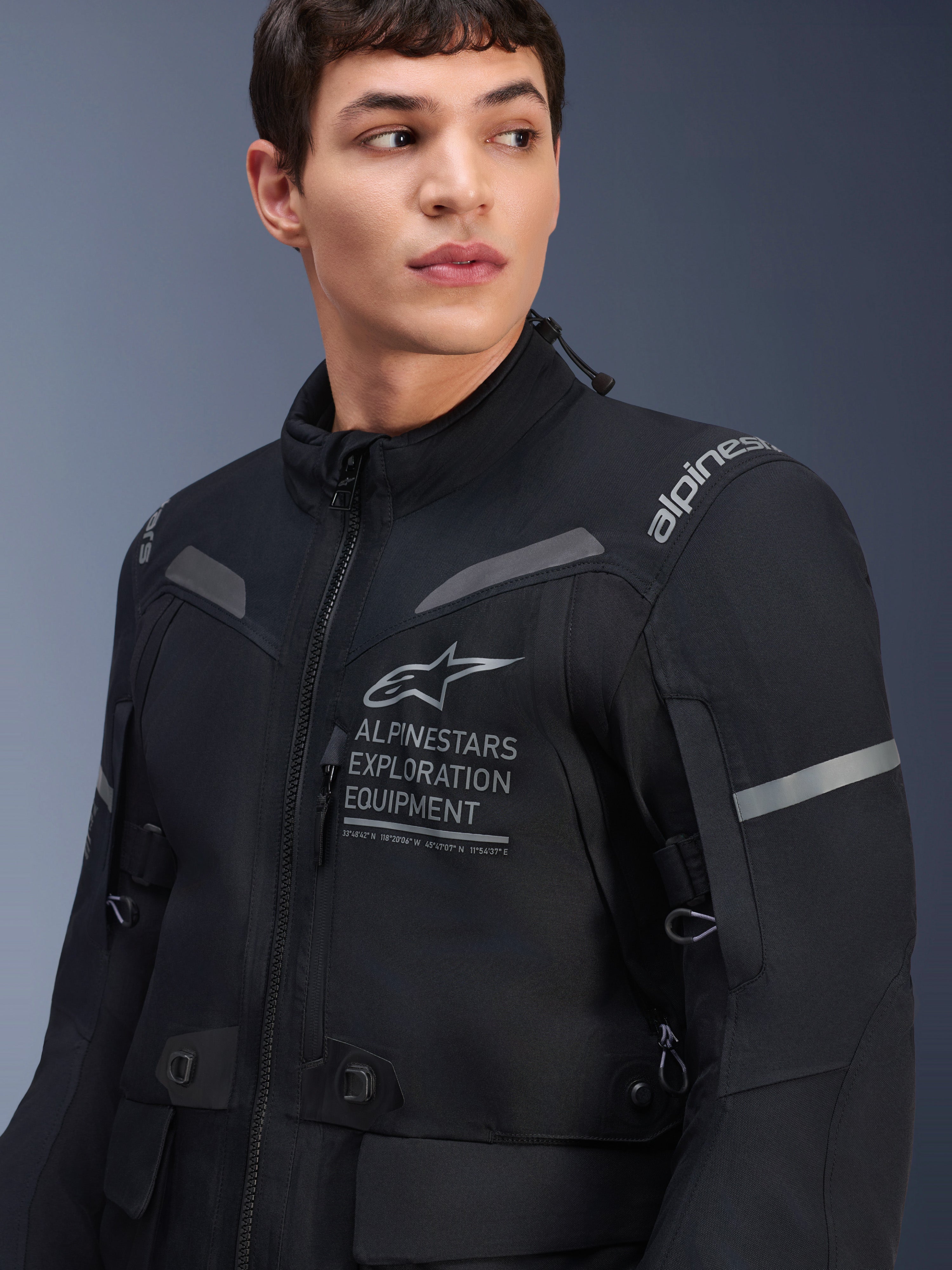Giacca Alpinestars ST-7 2L GORE-TEX, giacca da moto, nero e grigio scuro, indossata da un modello, con marchio Alpinestars Exploration Equipment sul petto, dettagli grigi riflettenti e struttura in tessuto pronta per l'avventura