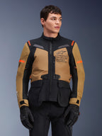 Giacca Alpinestars ST-7 2L GORE-TEX, giacca da moto adventure touring, marrone Gobi e nero con accenti arancioni, indossata da un modello, con marchio Exploration Equipment e tecnologia GORE-TEX, abbigliamento da moto impermeabile e resistente