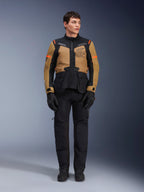 Modello che indossa la giacca Alpinestars ST-7 2L GORE-TEX, colore Gobi Brown e nero, abbigliamento moto adventure con pantaloni e guanti neri coordinati, logo Alpinestars Exploration Equipment sul petto, design impermeabile per touring su strada e fuoristrada