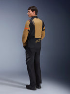 Giacca Alpinestars ST-7 2L GORE-TEX, giacca da moto adventure, Gobi Brown e nero, vista posteriore su un modello che indossa pantaloni e stivali da moto coordinati, con dettagli arancioni sulle maniche, guscio laminato impermeabile e logo Alpinestars, progettata per il touring e la guida su strada