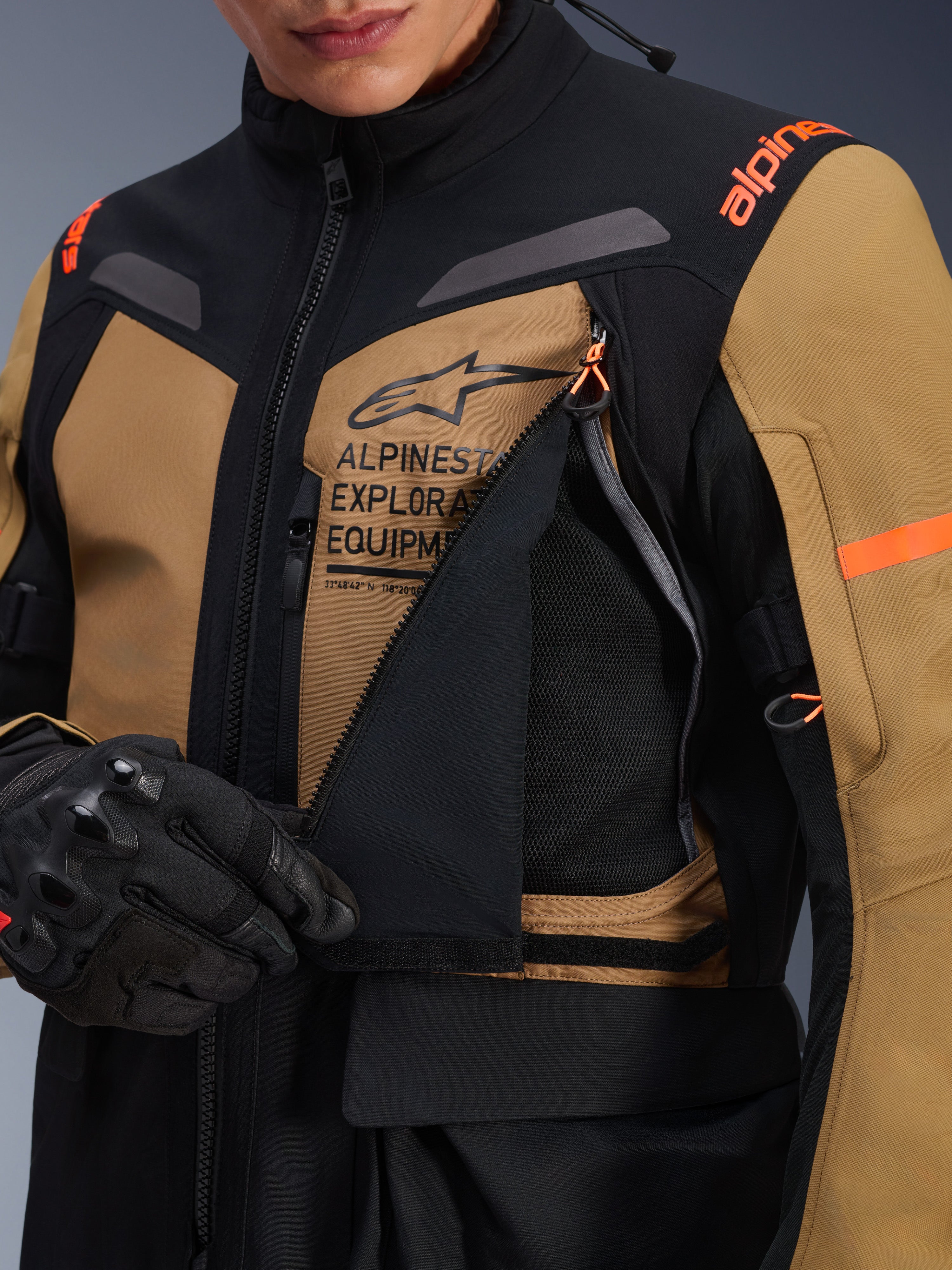Giacca Alpinestars ST-7 2L GORE-TEX, giacca da moto adventure touring, Gobi Brown e nero, primo piano del pannello di ventilazione sul petto aperto che rivela la rete traspirante, con marchio Alpinestars Exploration Equipment e accenti arancioni