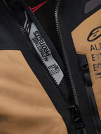 Dettaglio ravvicinato della giacca Alpinestars ST-7 2L GORE-TEX in Gobi Brown e nero, con i marchi 'ALPINESTARS PROTECTS' e 'TECH-AIR READY' all'interno della cerniera principale, robusta costruzione tessile e loghi sul petto