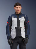 Giacca Alpinestars ST-7 2L GORE-TEX, giacca da moto adventure touring, grigio ghiaccio e blu scuro con dettagli rossi, impermeabile e traspirante, indossata da un modello con guanti neri, con logo Alpinestars Exploration Equipment sul petto