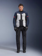 Giacca Alpinestars ST-7 2L GORE-TEX, giacca da moto Adventure Touring, Grigio Ghiaccio, Blu Scuro e Nero, indossata con pantaloni e guanti neri, dotata di ampie tasche cargo anteriori, dettagli rossi sulle maniche e guscio in GORE-TEX laminato per prestazioni impermeabili.