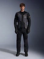 Modello che indossa la giacca Alpinestars ST-7 2L GORE-TEX in Deep Gray Black Dark Khaki, con il marchio 'ALPINESTARS EXPLORATION EQUIPMENT' sul petto, abbinata a pantaloni da moto, guanti e stivali neri coordinati, vista frontale in studio.