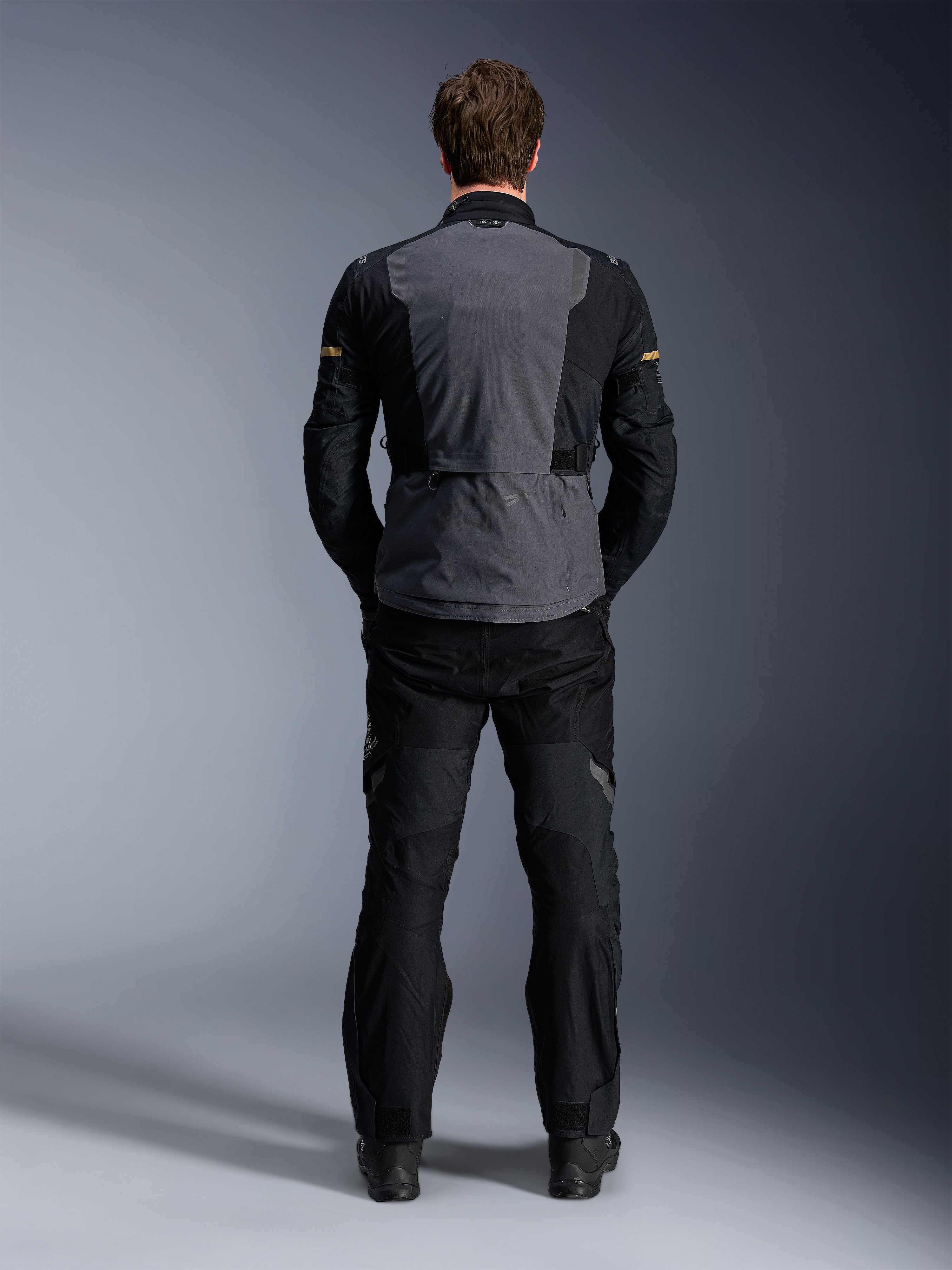 Giacca Alpinestars ST-7 2L GORE-TEX, Deep Gray Black e Dark Khaki, vista posteriore su un modello, giacca da moto adventure touring con pannello posteriore grigio e maniche articolate nere, indossata con pantaloni neri coordinati.