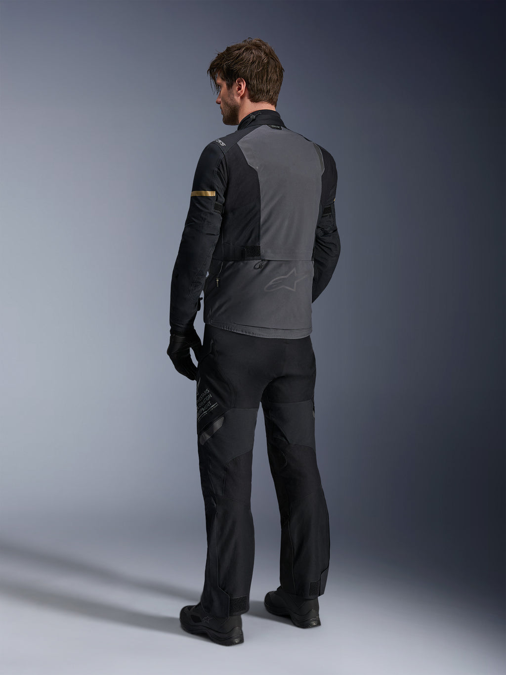 Giacca Alpinestars ST-7 2L GORE-TEX, Deep Gray e nero con accenti Dark Khaki, vista posteriore di un pilota che indossa la giacca e i pantaloni da moto coordinati, abbigliamento adventure touring con costruzione laminata impermeabile