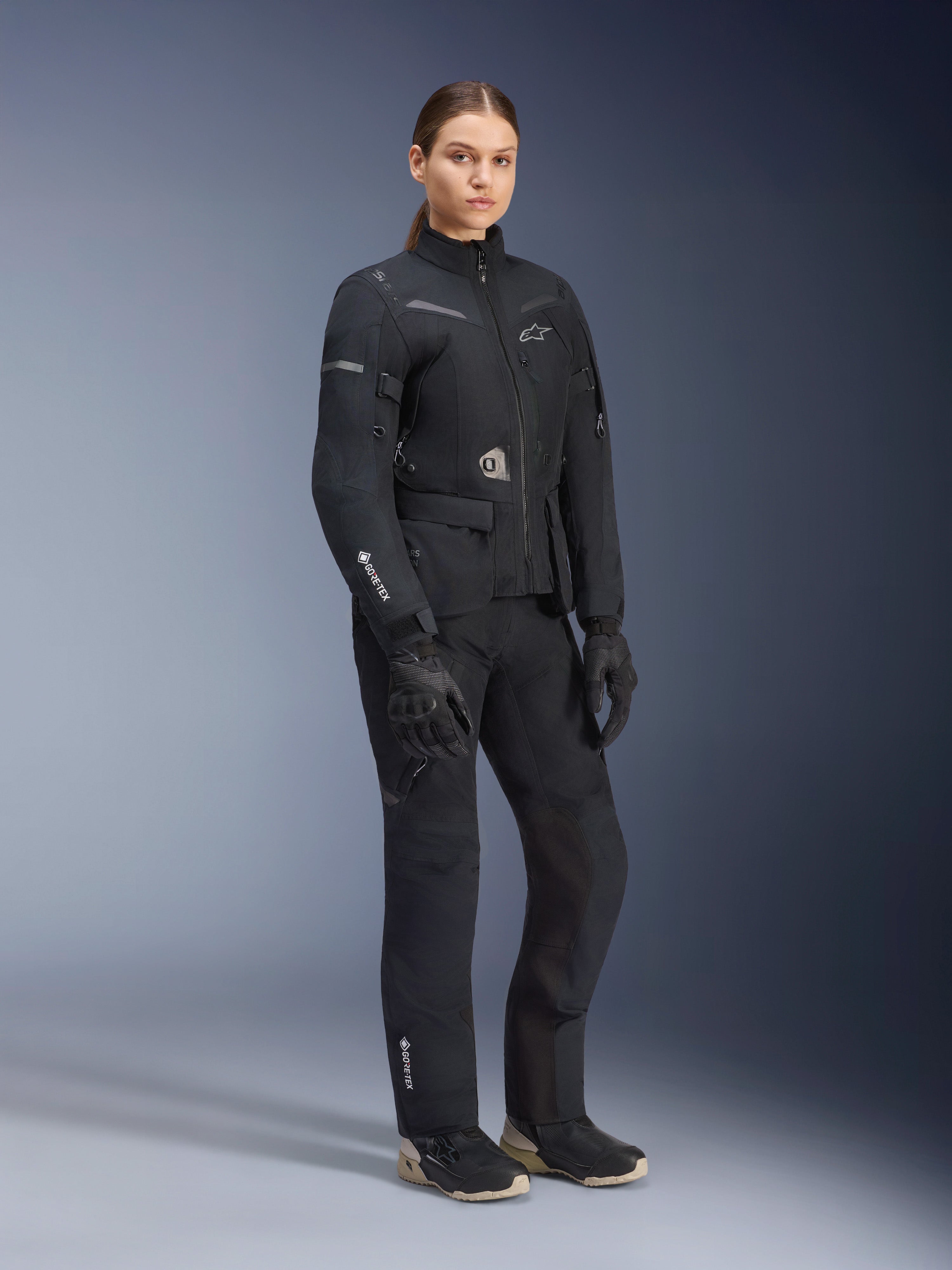Giacca Alpinestars Stella ST-7 2L GORE-TEX da donna, nero, indossata con pantaloni da moto e guanti abbinati, equipaggiamento adventure road-touring con marchio GORE-TEX laminato sulla manica e vestibilità femminile sagomata.