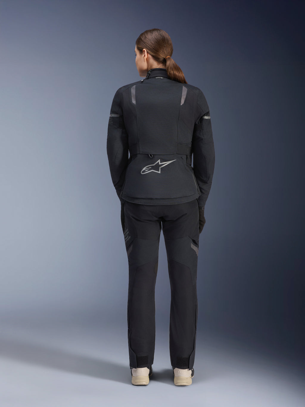 Giacca Alpinestars Stella ST-7 2L GORE-TEX da donna, nero e grigio scuro, vista posteriore con logo Alpinestars argento sulla parte bassa della schiena, abbinata a pantaloni in tessuto neri coordinati, abbigliamento moto adventure touring