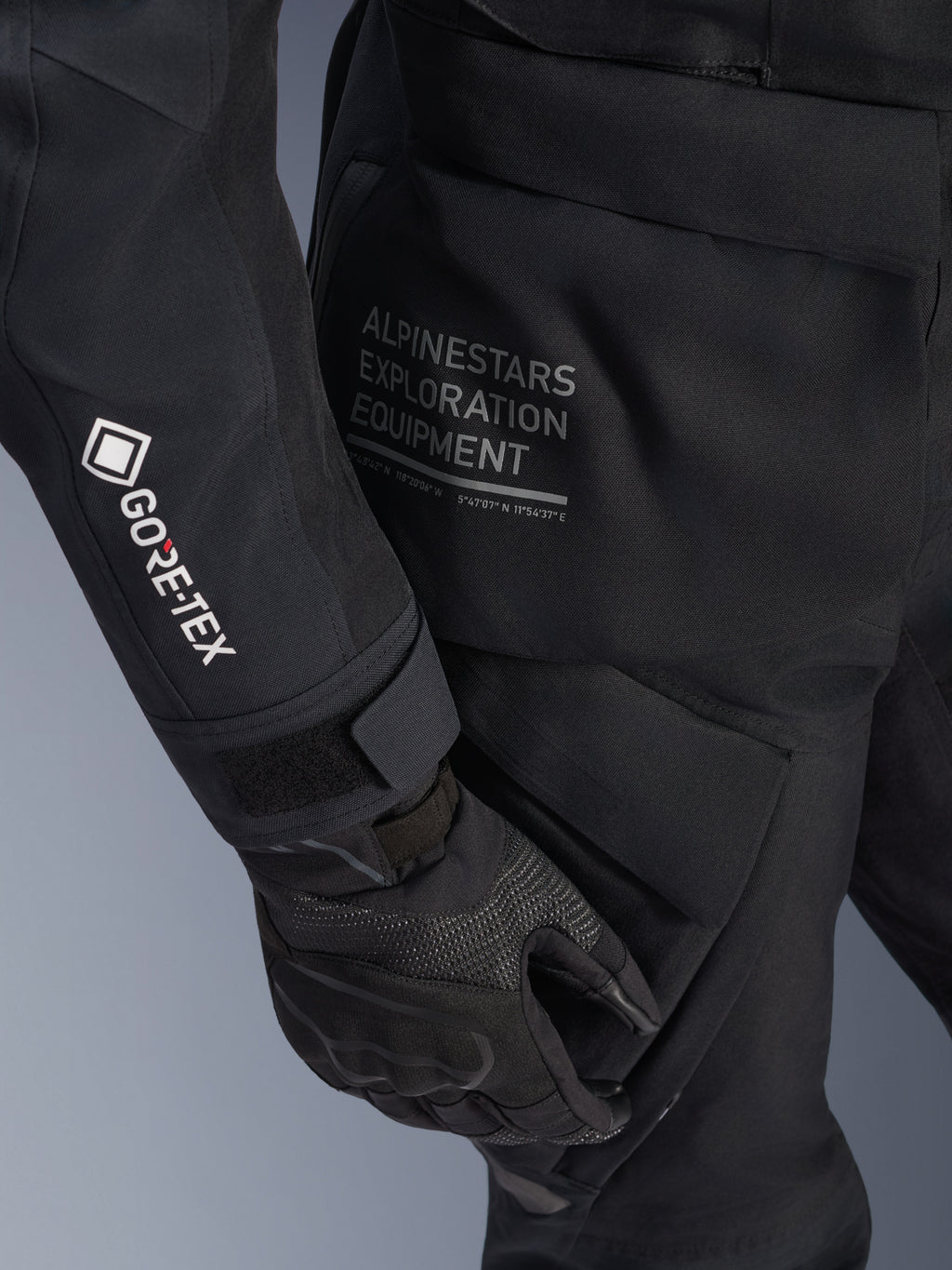 Giacca Alpinestars Stella ST-7 2L GORE-TEX da donna, giacca da moto adventure touring nera, vista ravvicinata della manica con logo GORE-TEX bianco, scritta Alpinestars Exploration Equipment sul fianco, guanto da moto nero, materiale tessile impermeabile con tasche cargo funzionali