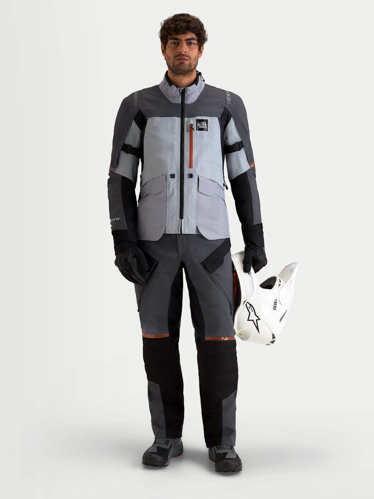 Alpinestars St 7 V 2 2 L Gore Tex Pantaloni, pantaloni da moto adventure touring da uomo, grigio scuro e nero, vista frontale su un modello che indossa l'equipaggiamento coordinato e tiene un casco