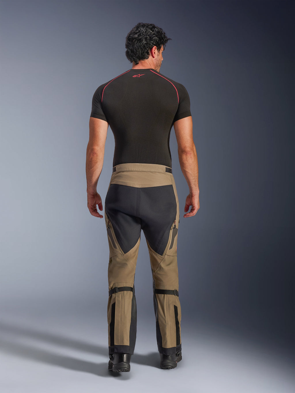 Pantaloni Alpinestars Nazca 3L GORE-TEX PRO, pantaloni da moto adventure Walnut Black, vista posteriore su un modello con base layer nero e stivali, design bicolore con regolatori del polpaccio e pannelli elasticizzati.