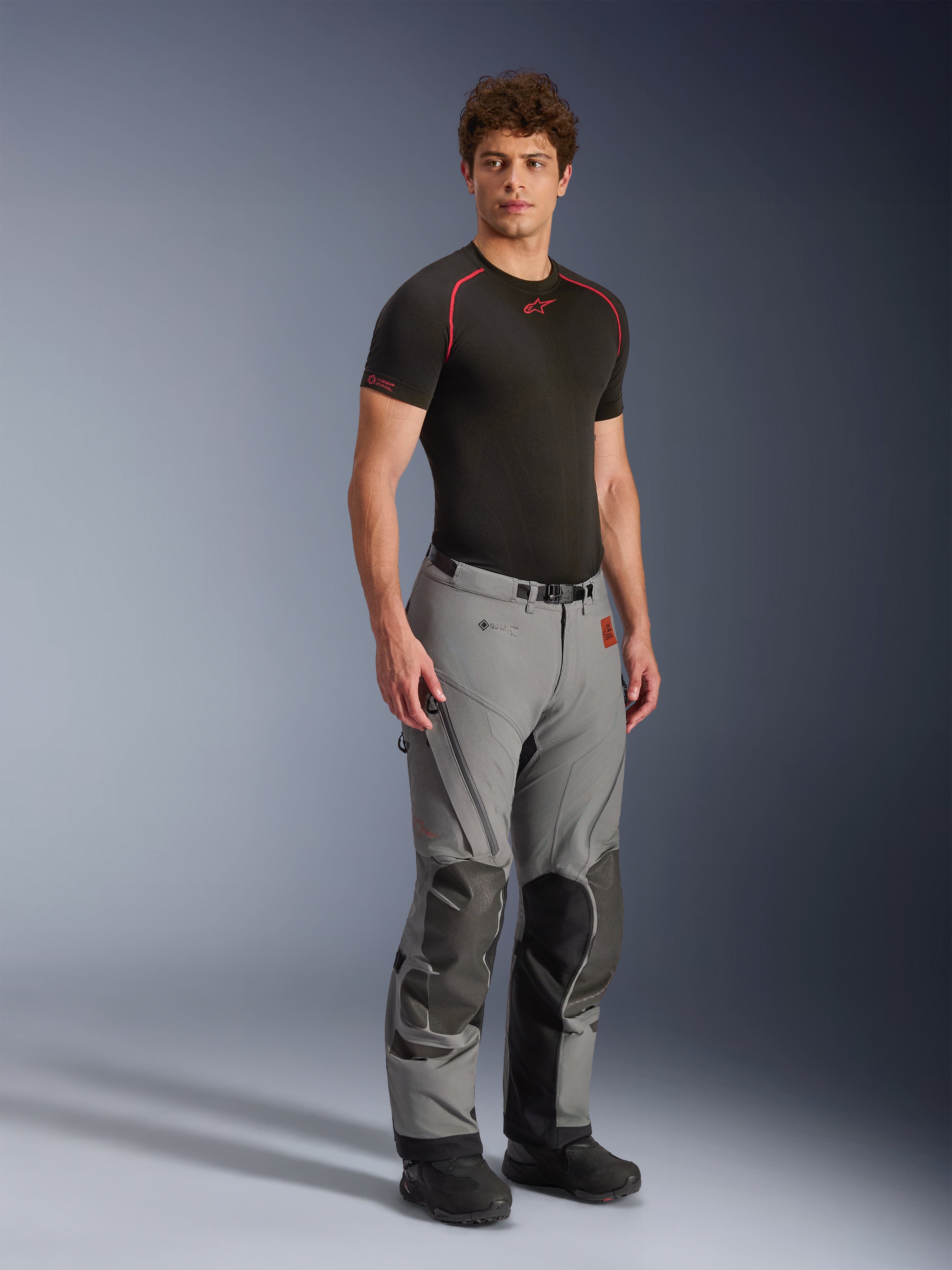 Modello che indossa i pantaloni Alpinestars Nazca 3L GORE-TEX PRO, pantaloni da moto adventure grigio scuro e nero, con pannelli rinforzati sulle ginocchia e ventilazione con zip, indossati con un top base layer nero, abbigliamento tecnico progettato per il riding estremo su ogni tipo di terreno.