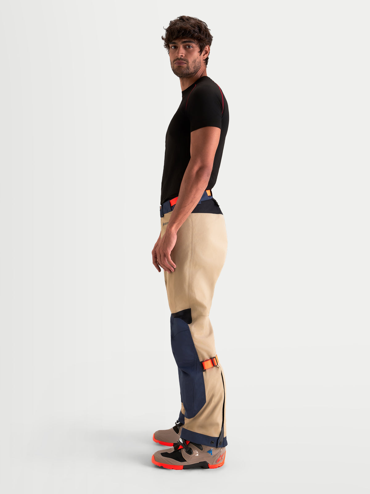 Alpinestars Arenis Gore-Tex Pantaloni, pantaloni da moto adventure da uomo in blu navy e alluminio, vista laterale indossati da un modello per mostrare la costruzione in tessuto impermeabile e i regolatori di vestibilità sulla parte inferiore della gamba