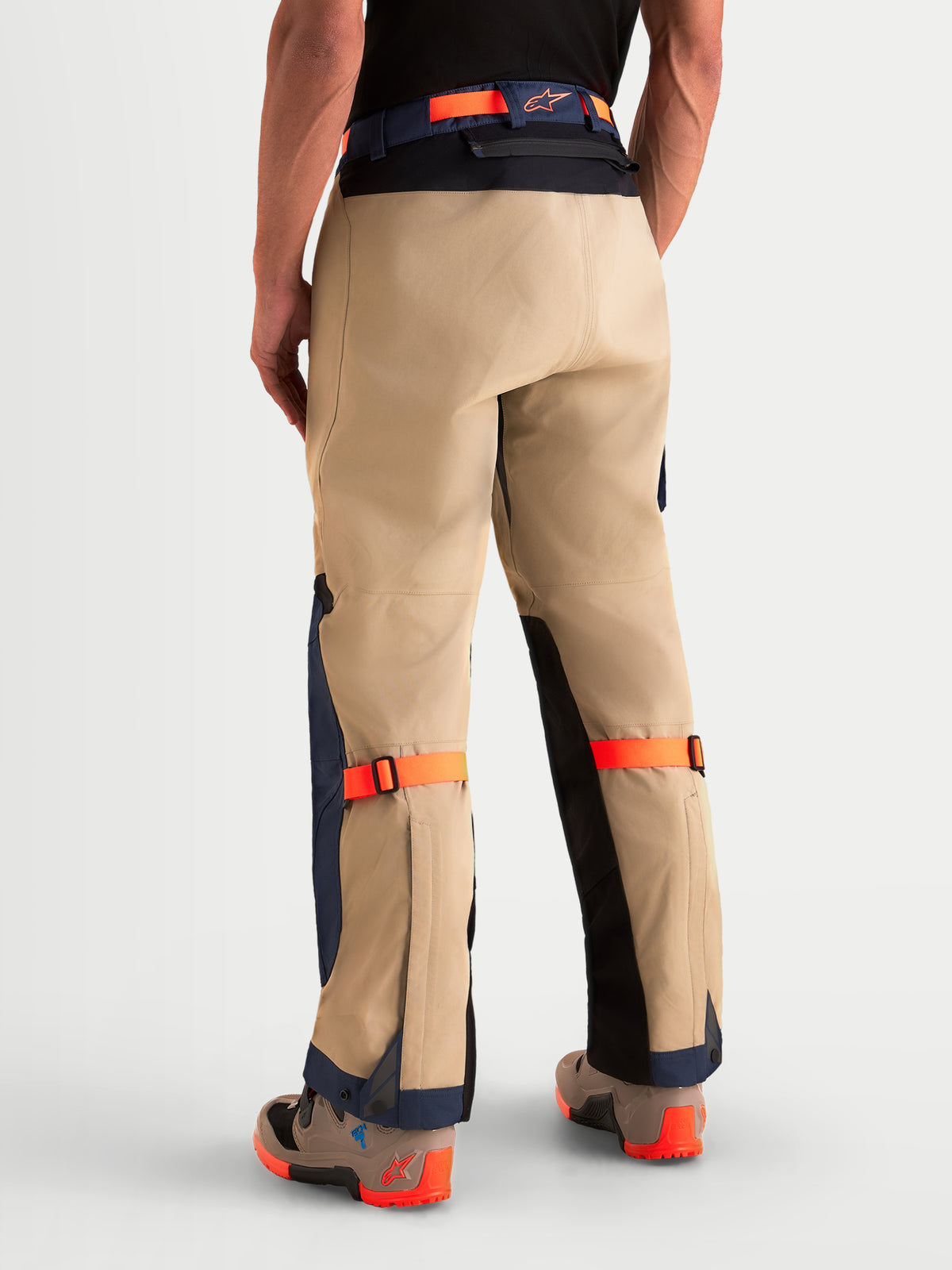 Alpinestars Arenis Gore Tex Pantaloni, pantaloni da moto adventure da uomo in beige, blu scuro e arancione, vista posteriore su un modello che mostra la struttura in tessuto impermeabile, seduta rinforzata e cinghie regolabili