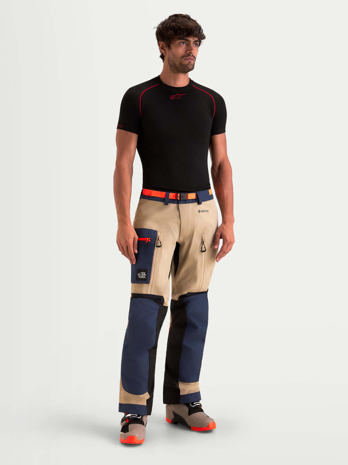 Alpinestars Arenis Gore-Tex Pantaloni, pantaloni da moto adventure da uomo in blu navy, beige e nero, vista frontale indossati da un modello con maglietta nera, con struttura impermeabile in GORE-TEX e tasca cargo
