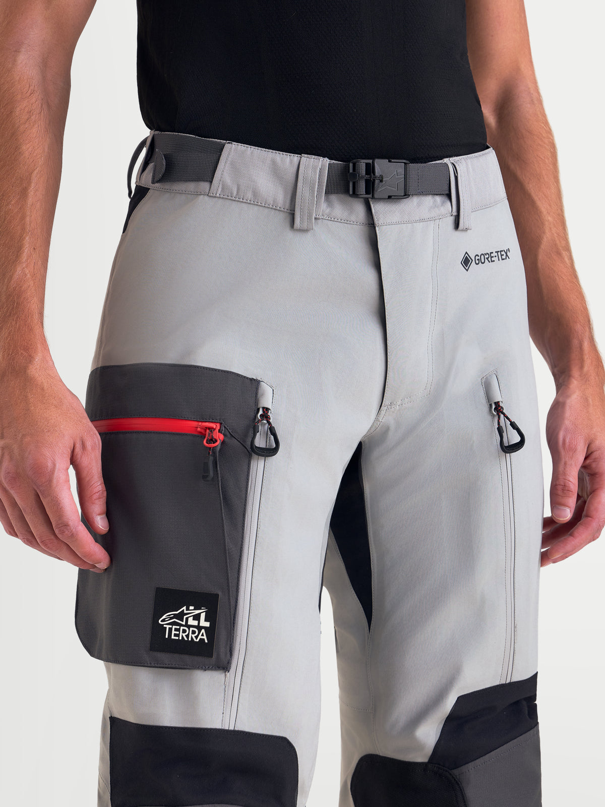 Alpinestars Arenis Gore-Tex Pantaloni, pantaloni da moto adventure da uomo in grigio medio, grigio scuro e nero, vista ravvicinata che mostra la fibbia magnetica in vita, il logo GORE-TEX, la ventilazione sulle cosce con zip e la tasca cargo indossati da un modello