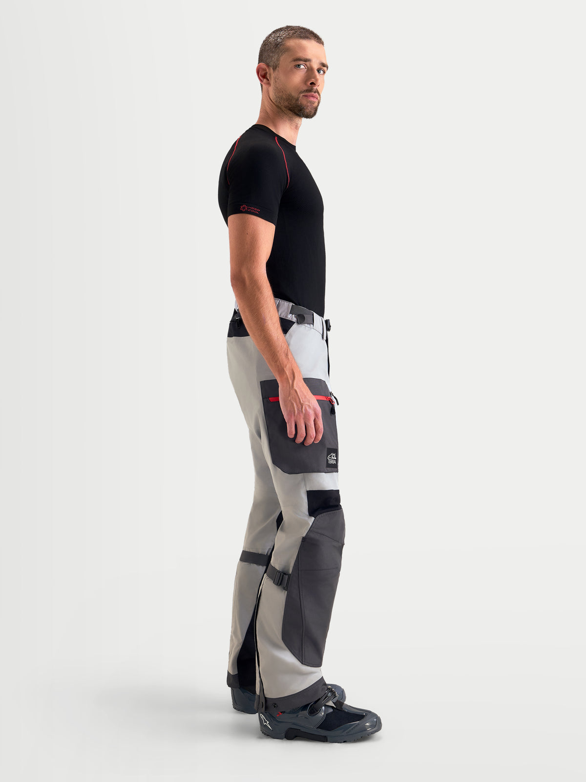 Alpinestars Arenis Gore-Tex Pantaloni, pantaloni da moto adventure da uomo in grigio medio, grigio scuro e nero, vista di profilo laterale che mostra la costruzione in tessuto impermeabile e la tasca cargo indossati da un modello