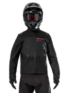 Alpinestars Pro-Dura Jacket, giacca da moto off-road nera, vista frontale indossata da un pilota con casco e occhiali neri abbinati, logo Alpinestars rosso, tasche pettorali con zip e costruzione in tessuto resistente per l'enduro
