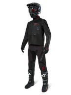 Pilota di motocross con abbigliamento completo da gara, Giacca Alpinestars Pro-Dura in nero, pantaloni neri con marchio grigio e accenti rossi, casco nero con maschera e stivali da motocross neri e bianchi, completo coordinato per enduro e guida fuoristrada