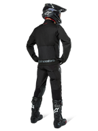 Giacca Alpinestars Pro-Dura, giacca da enduro off-road nera, vista posteriore indossata con pantaloni coordinati e stivali Tech 10 neri, caratterizzata dal prominente logo Alpinestars sulla parte bassa della schiena, costruzione in tessuto robusto per guida trail aggressiva
