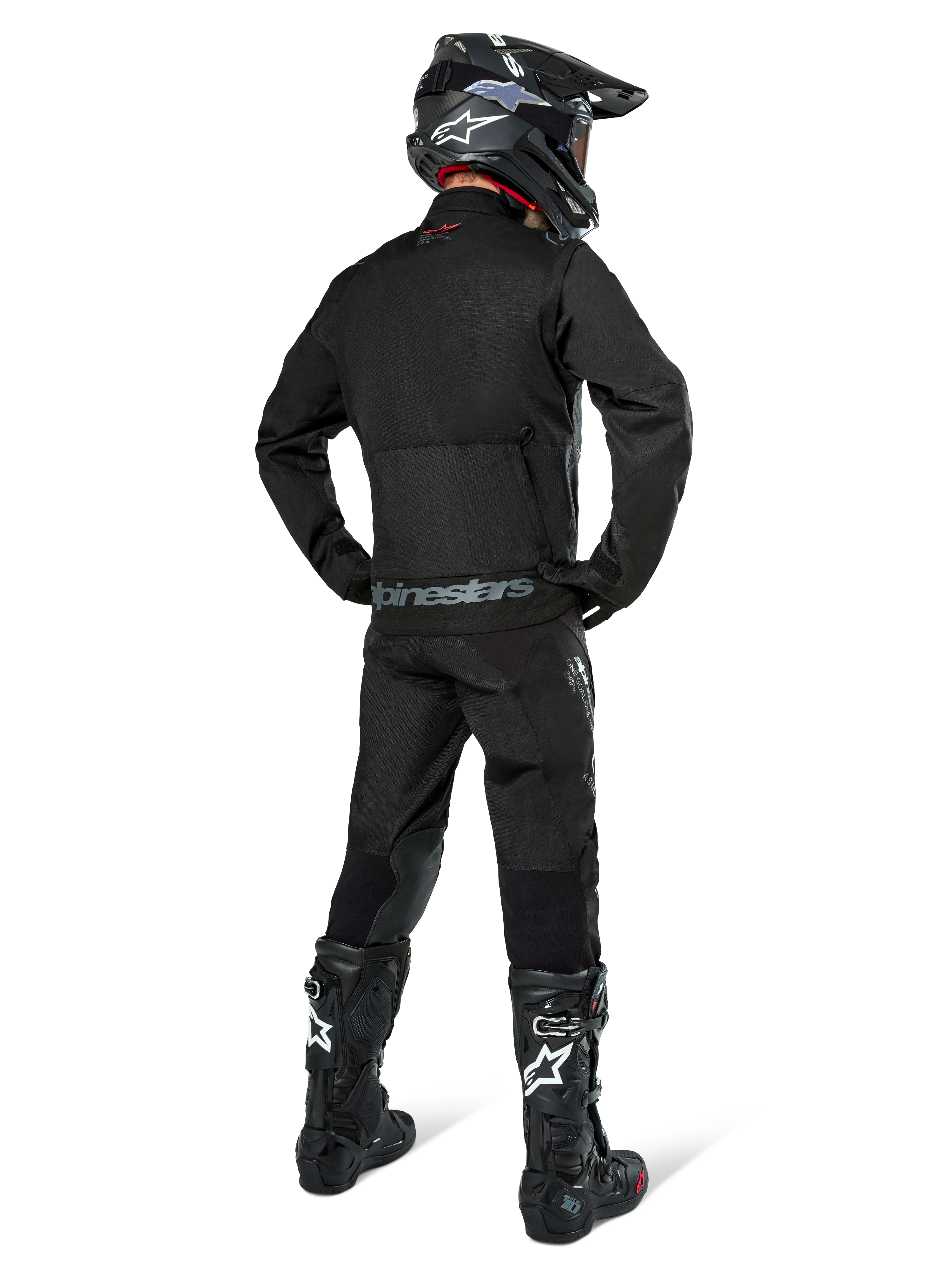 Giacca Alpinestars Pro-Dura, giacca da enduro off-road nera, vista posteriore indossata con pantaloni coordinati e stivali Tech 10 neri, caratterizzata dal prominente logo Alpinestars sulla parte bassa della schiena, costruzione in tessuto robusto per guida trail aggressiva