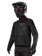 Alpinestars Pro-Dura Jacket, giacca da moto off-road, nera con loghi rossi e grigi, tasche anteriori con zip e colletto alto, indossata con casco da motocross e guanti neri per gare di enduro