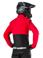 Giacca Alpinestars Pro-Dura, giacca da enduro fuoristrada, rossa e nera con logo Alpinestars bianco sull'orlo posteriore, indossata da un pilota visto da dietro con un casco da motocross nero, design ispirato al rally per una guida aggressiva su sentieri