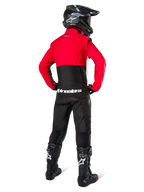 Pilota di motocross visto da dietro che indossa la Giacca Alpinestars Pro-Dura in nero, rosso acceso e bianco, abbinata a pantaloni neri, casco nero e stivali da fuoristrada neri, caratterizzata da una parte superiore rossa e una inferiore nera con logo Alpinestars bianco sulla schiena.