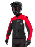 Giacca Alpinestars Pro-Dura, giacca da moto enduro fuoristrada, nero con blocchi di colore rosso acceso e bianco, indossata da un pilota con casco nero e maschera, dotata di tasche anteriori con zip e logo Alpinestars, struttura in tessuto resistente per trail riding