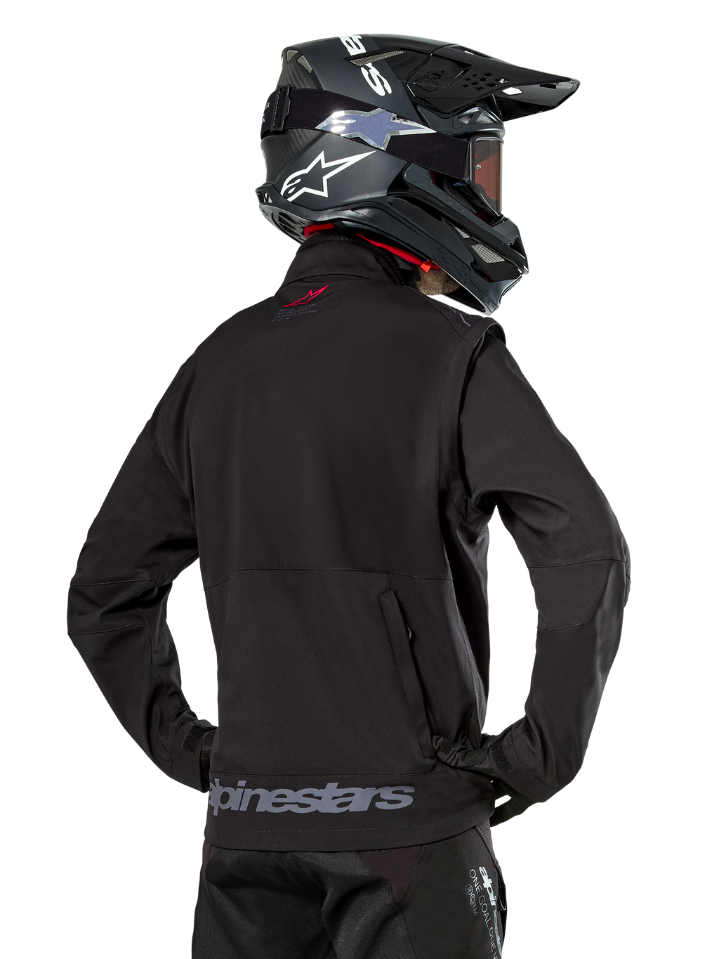 Giacca Alpinestars Lite-Dura Softshell, nero, vista posteriore indossata da un pilota, con branding Alpinestars grigio sull'orlo posteriore e un piccolo logo rosso sul colletto, abbinata a un casco da motocross nero, progettata per l'enduro e il fuoristrada