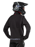 Giacca Alpinestars Lite-Dura Softshell, nero, vista posteriore indossata da un pilota, con branding Alpinestars grigio sull'orlo posteriore e un piccolo logo rosso sul colletto, abbinata a un casco da motocross nero, progettata per l'enduro e il fuoristrada