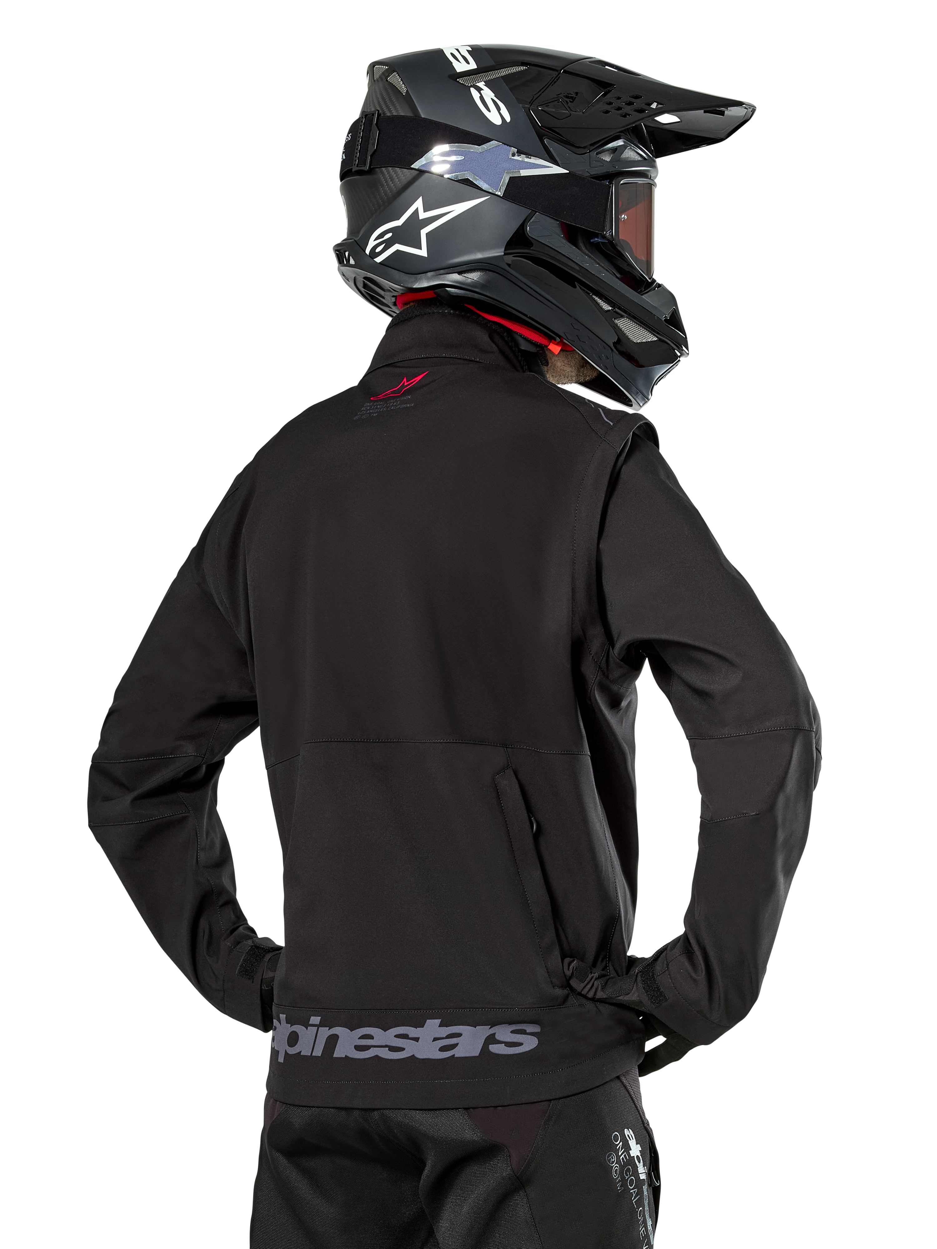 Giacca Alpinestars Lite-Dura Softshell, nero, vista posteriore indossata da un pilota, con branding Alpinestars grigio sull'orlo posteriore e un piccolo logo rosso sul colletto, abbinata a un casco da motocross nero, progettata per l'enduro e il fuoristrada