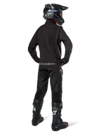 Pilota di enduro visto di schiena con la giacca Softshell Alpinestars Lite-Dura in nero, abbinata a pantaloni tecnici e stivali neri, con tasca posteriore con zip e logo Alpinestars sull'orlo inferiore, equipaggiamento completo off-road per motocross.