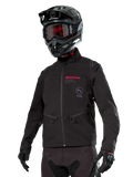 Alpinestars Lite-Dura Softshell Jacket, giacca da moto off-road nera con logo rosso e logo AS, indossata con casco da motocross nero, maschera rossa e guanti neri, dotata di tasche con zip e polsini regolabili, ideale per l'enduro