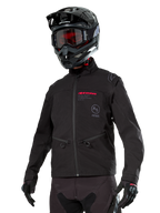 Alpinestars Lite-Dura Softshell Jacket, giacca da moto off-road nera con logo rosso e logo AS, indossata con casco da motocross nero, maschera rossa e guanti neri, dotata di tasche con zip e polsini regolabili, ideale per l'enduro
