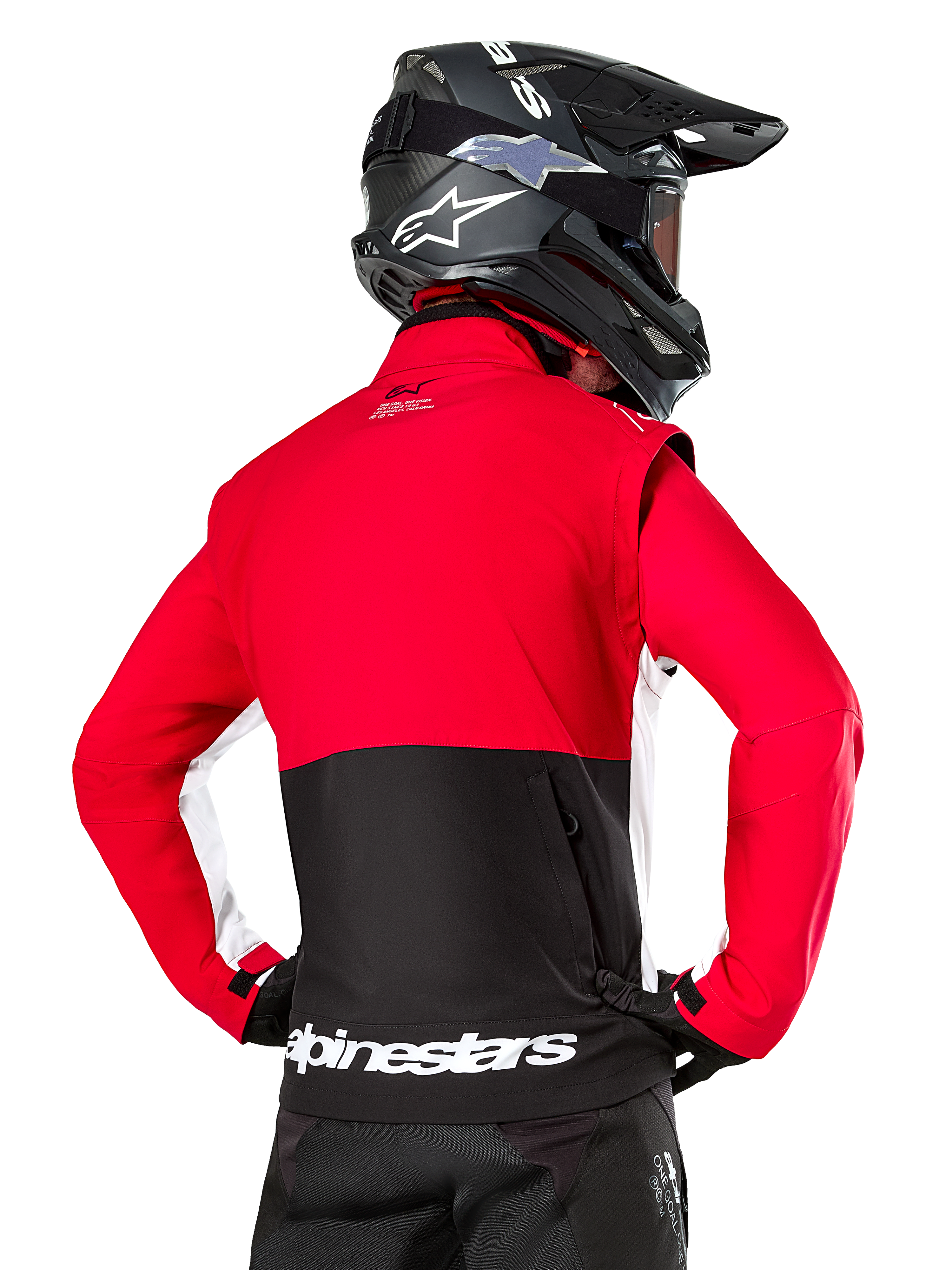 Alpinestars Lite-Dura Softshell Jacket, nero, rosso brillante e bianco, vista posteriore su un pilota di motocross, parte superiore e maniche rosse con pannello posteriore inferiore nero, tasca posteriore portaoggetti con zip, logo Alpinestars bianco sull'orlo inferiore, indossata con casco e pantaloni neri.