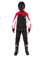 Pilota di motocross con Giacca Alpinestars Lite-Dura Softshell in nero, rosso brillante e bianco, coordinata con pantaloni off-road neri, stivali neri e bianchi e casco nero con occhiali, equipaggiamento completo per gare di enduro