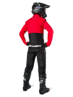 Pilota di motocross da dietro con giacca Softshell Alpinestars Lite-Dura, nero rosso acceso e bianco, con pannello superiore rosso e sezione inferiore nera con branding bianco, abbinata a pantaloni neri, casco nero e stivali neri, completo da enduro coordinato per guida off-road