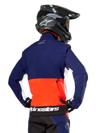 Giacca Softshell Alpinestars Lite-Dura, blu navy, arancione acceso e bianco, vista posteriore indossata da un pilota di motocross, con un grande logo bianco sull'orlo posteriore e tasca portaoggetti con zip, parte di un completo da gara off-road