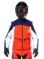 Giacca Softshell Alpinestars Lite-Dura in blu navy, arancione acceso e bianco, vista frontale su un pilota con casco nero e maschera, design tecnico color-block con tasche con zip e logo Alpinestars, attrezzatura versatile per enduro e fuoristrada