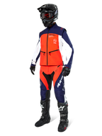 Pilota di motocross con giacca softshell Alpinestars Lite-Dura in blu navy, arancione e bianco, pantaloni da fuoristrada coordinati, casco nero con maschera e stivali da gara neri, set di abbigliamento da enduro coordinato