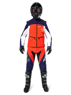 Pilota di motocross con equipaggiamento completo da fuoristrada, Giacca Softshell Lite-Dura in blu navy, arancione acceso e bianco, pantaloni coordinati blu navy e arancione, casco nero con occhiali, stivali bianchi e neri, guanti neri, outfit coordinato per gare di enduro