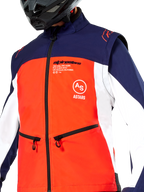 Giacca Softshell Alpinestars Lite-Dura, blu navy, arancione acceso e bianco, vista ravvicinata del torso, pannello frontale arancione con fianchi bianchi e spalle blu navy, tasche con zip e logo Alpinestars, indossata con casco da fuoristrada nero