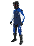 Giacca Softshell Alpinestars Lite-Dura, blu navy, azzurro e bianco, indossata con pantaloni da fuoristrada coordinati, stivali da motocross neri, casco nero con occhiali e guanti neri, equipaggiamento completo da enduro per gare fuoristrada