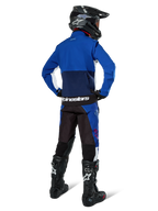 Pilota di motocross visto di spalle che indossa la giacca Alpinestars Lite-Dura Softshell in Navy Bright Blue e bianco, abbinata a pantaloni da enduro coordinati, casco nero e stivali neri, abbigliamento completo da gara off-road