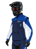 Giacca Softshell Alpinestars Lite-Dura, blu navy, azzurro e bianco, giacca da enduro off-road, indossata con casco nero e occhiali con lenti rosse, design sportivo color-block con cerniere multiple e loghi del brand, tessuto resistente per motocross e trail riding